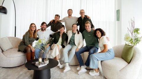 Het team van Maximum Image, samen gefotografeerd op lichte fauteuils en een bank in een heldere loungeruimte.